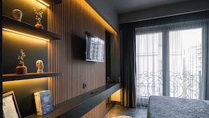 Une chambre d’hôtel moderne dotée d’un grand lit, d’un téléviseur fixé au mur, d’un mur recouvert de panneaux en bois et d’un balcon agrémenté d’une rambarde en fer forgé.