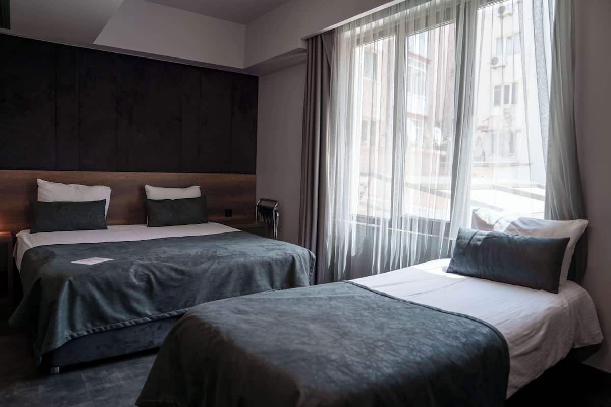 Een hotelkamer met twee bedden, een groot raam met dunne gordijnen en een donker houten hoofdeinde.
