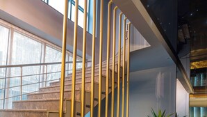 Un intérieur moderne avec un escalier en marbre, des rampes en verre et des plantes en pot.