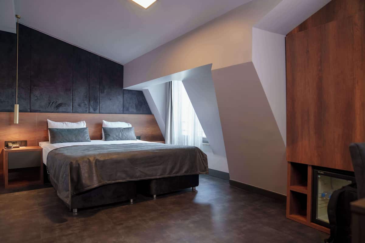 Een moderne slaapkamer met een groot bed, nachtkastje, houten hoofdbord en een ingebouwde televisie.