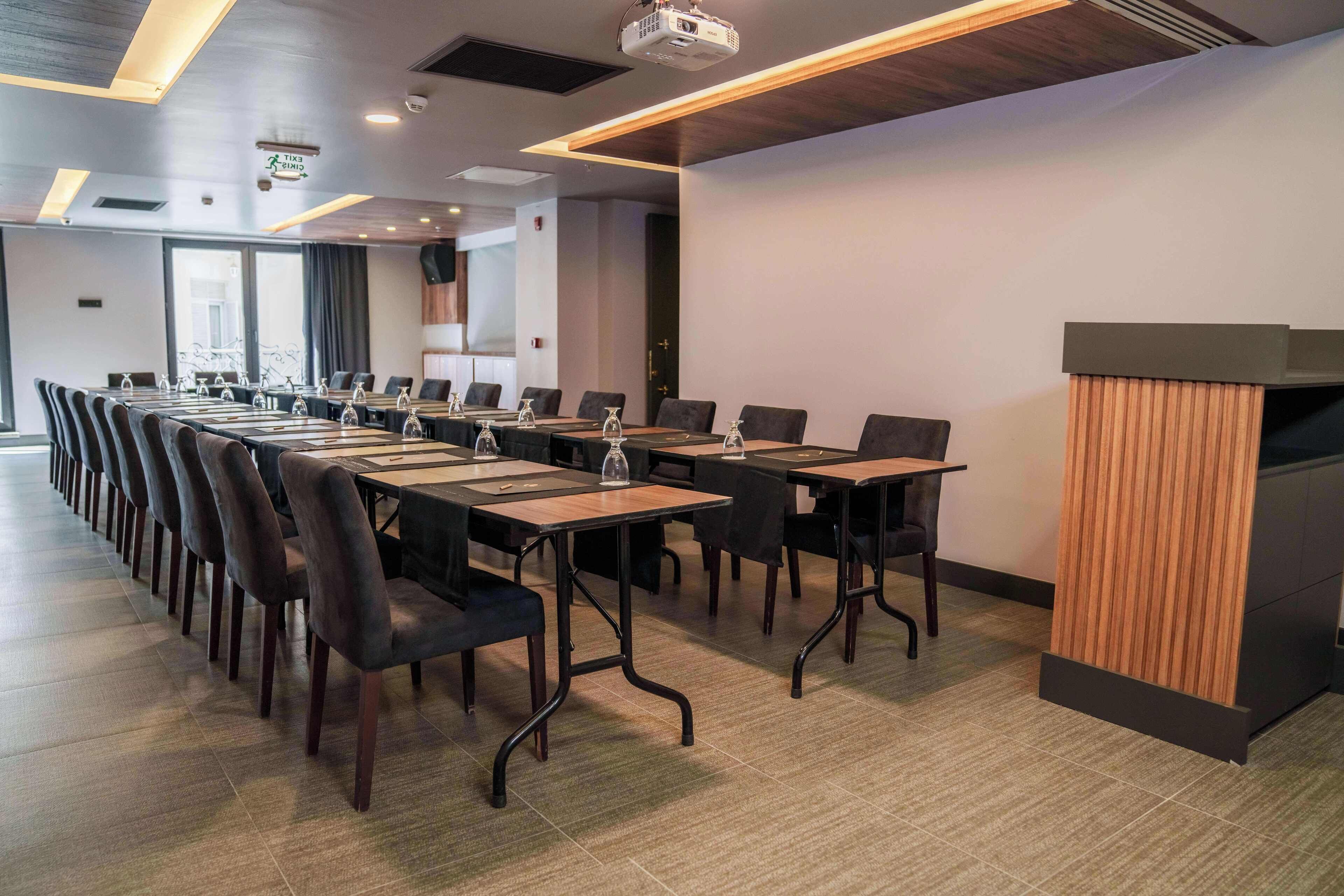 Un salón de conferencias con largas mesas y sillas, un atril y un proyector.