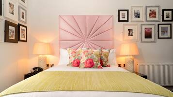 A neatly arranged bedroom with a large bed, two bedside lamps, a decorative headboard, and a series of framed pictures on the wall.