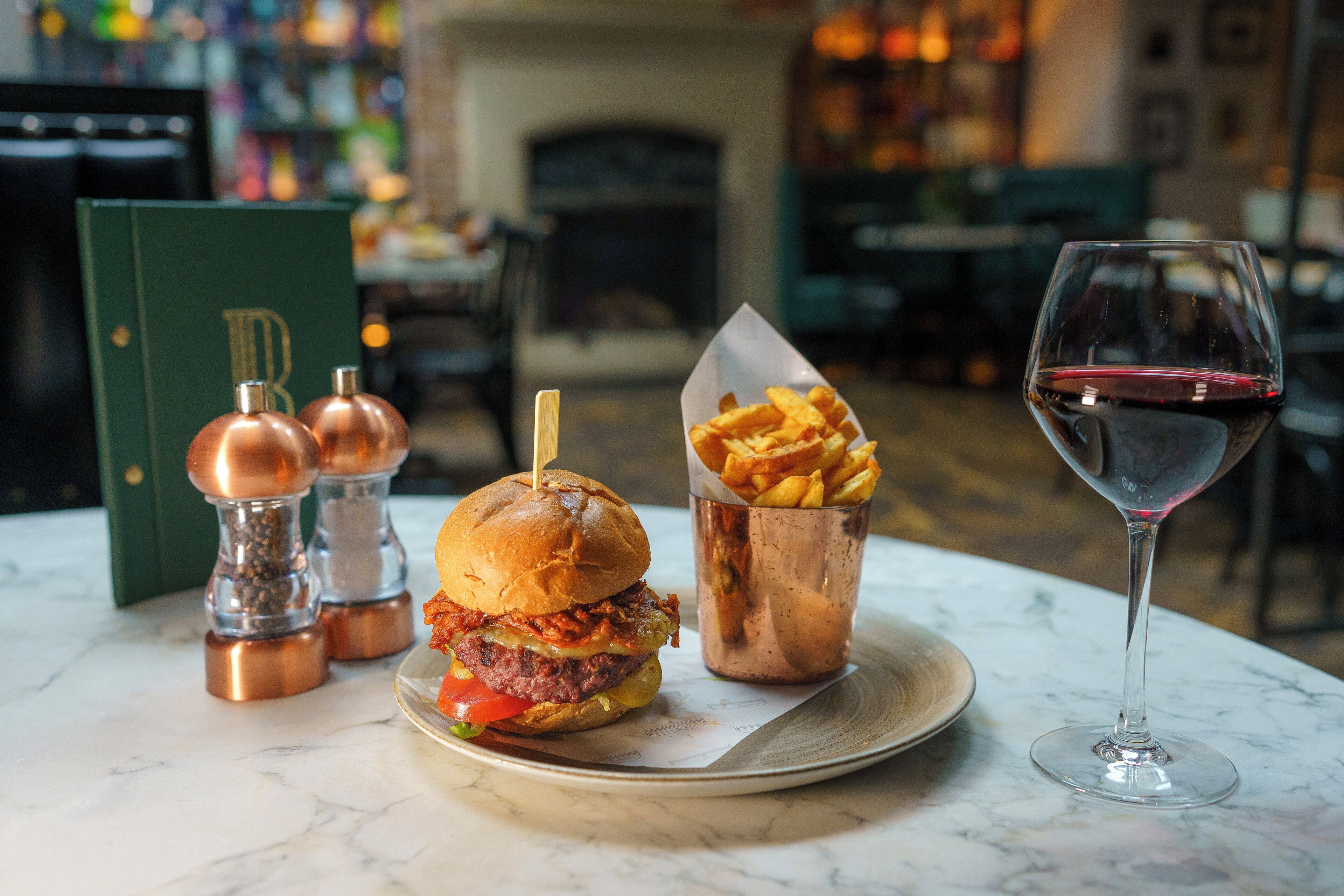 Una hamburguesa, papas fritas y una copa de vino tinto sobre una mesa.