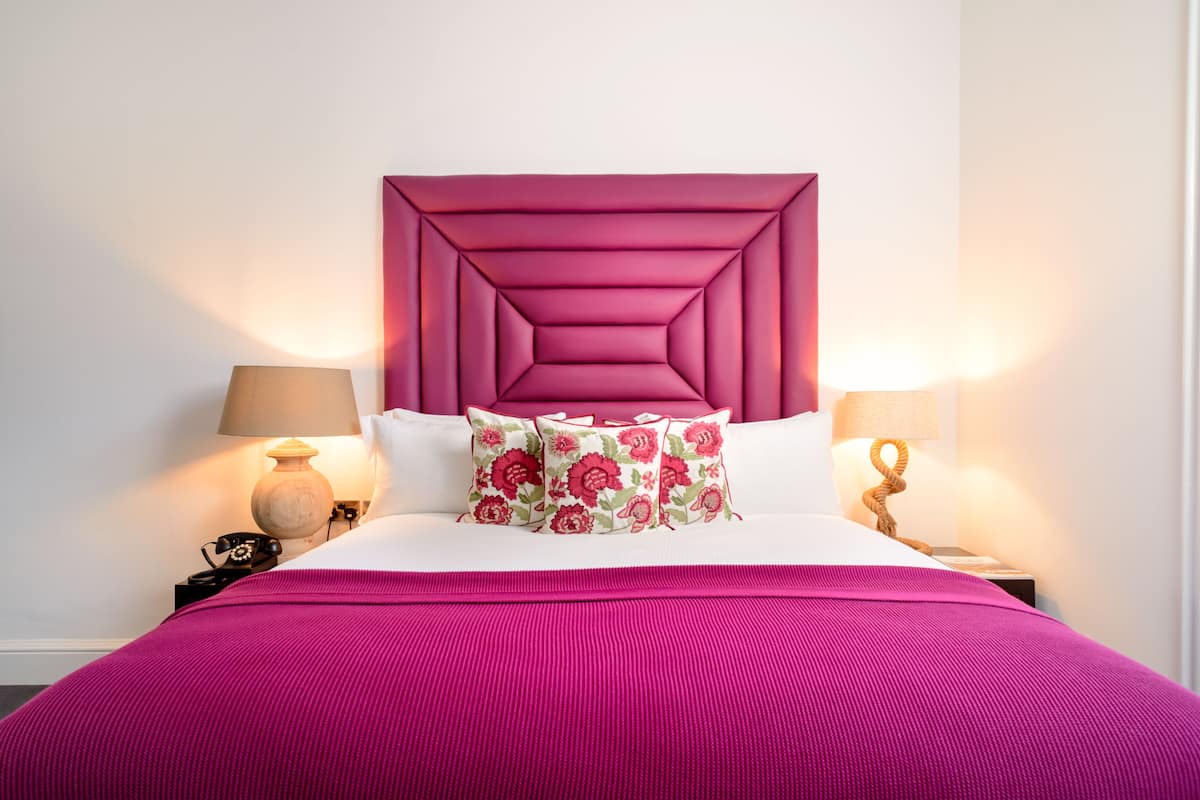A bed with a pink headboard, floral pillows, and a pink bedspread.