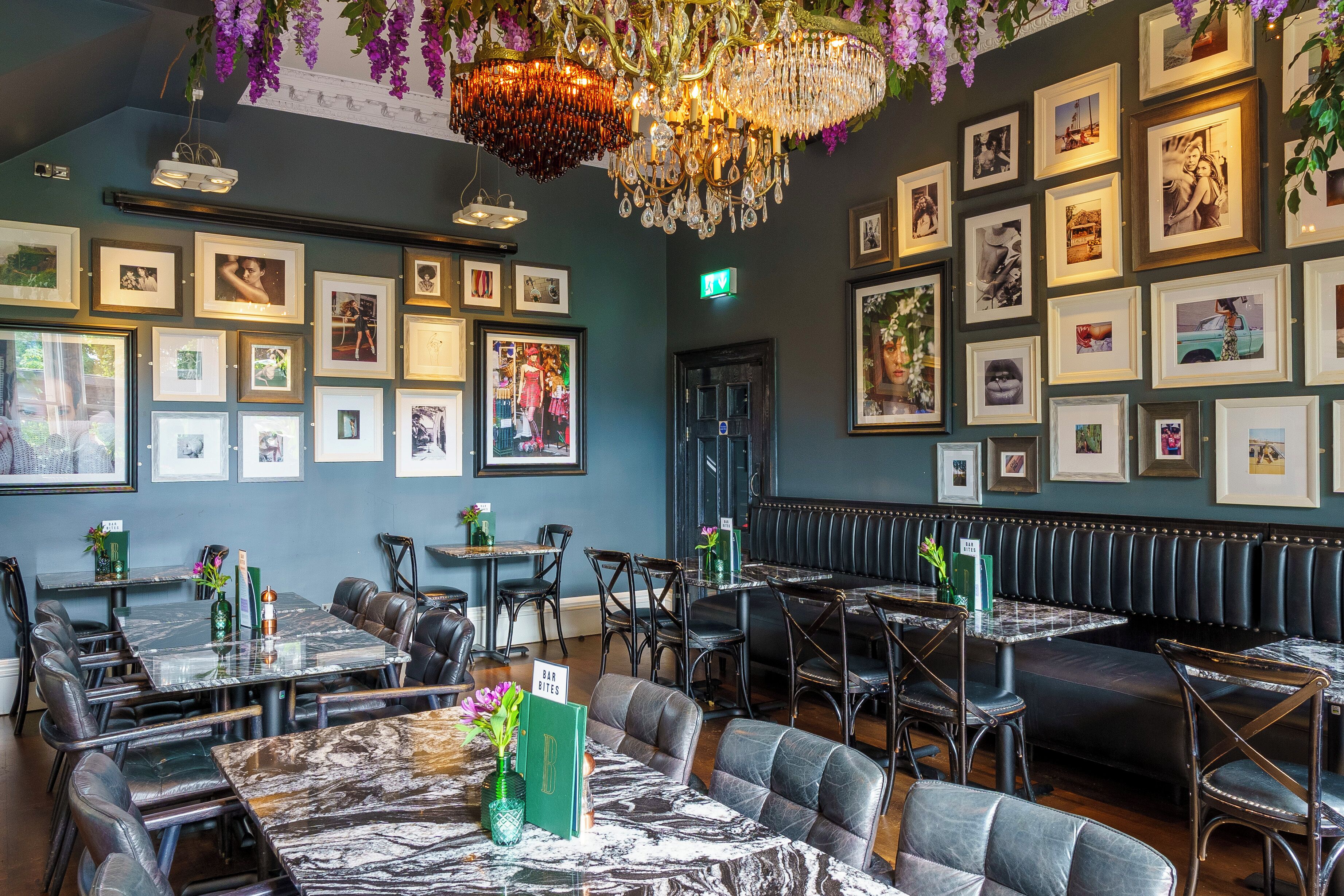 A restaurant with marble-topped tables and black leather booths, framed pictures on the walls, and a chandelier.
