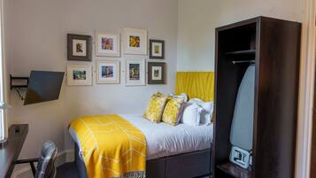 A bedroom with a bed, a desk, a chair, a wardrobe, and framed pictures on the wall.