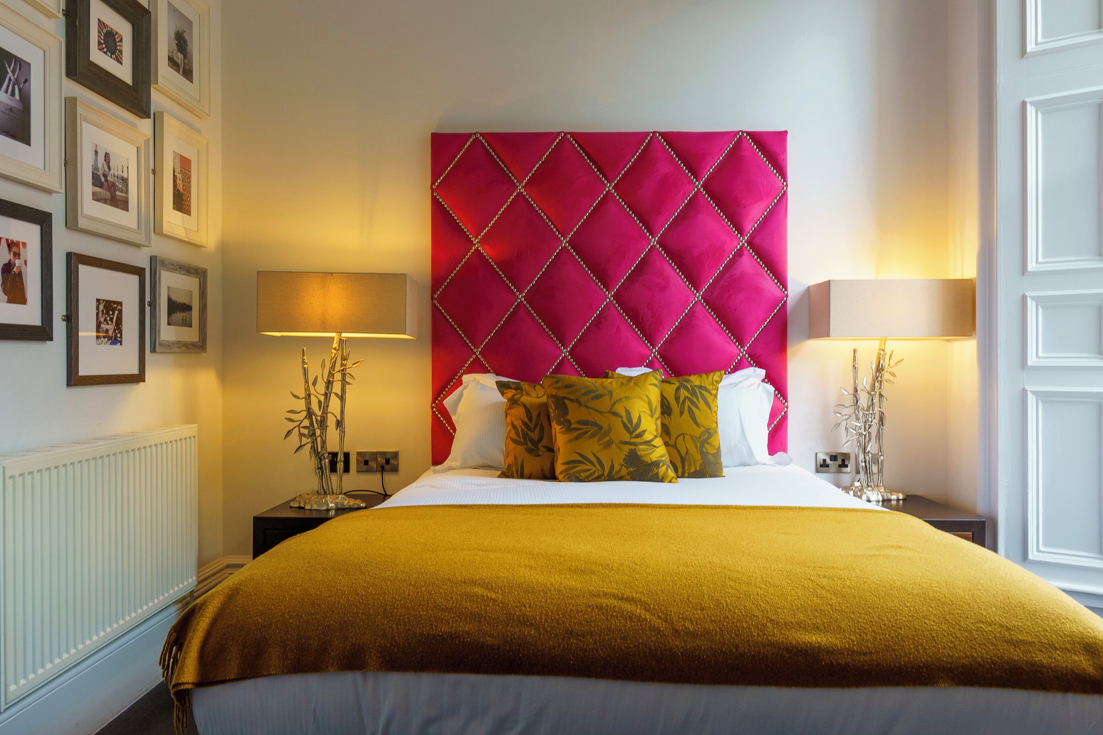 Una habitación de hotel con una cama grande, un cabecero rojo y cuadros enmarcados en la pared.