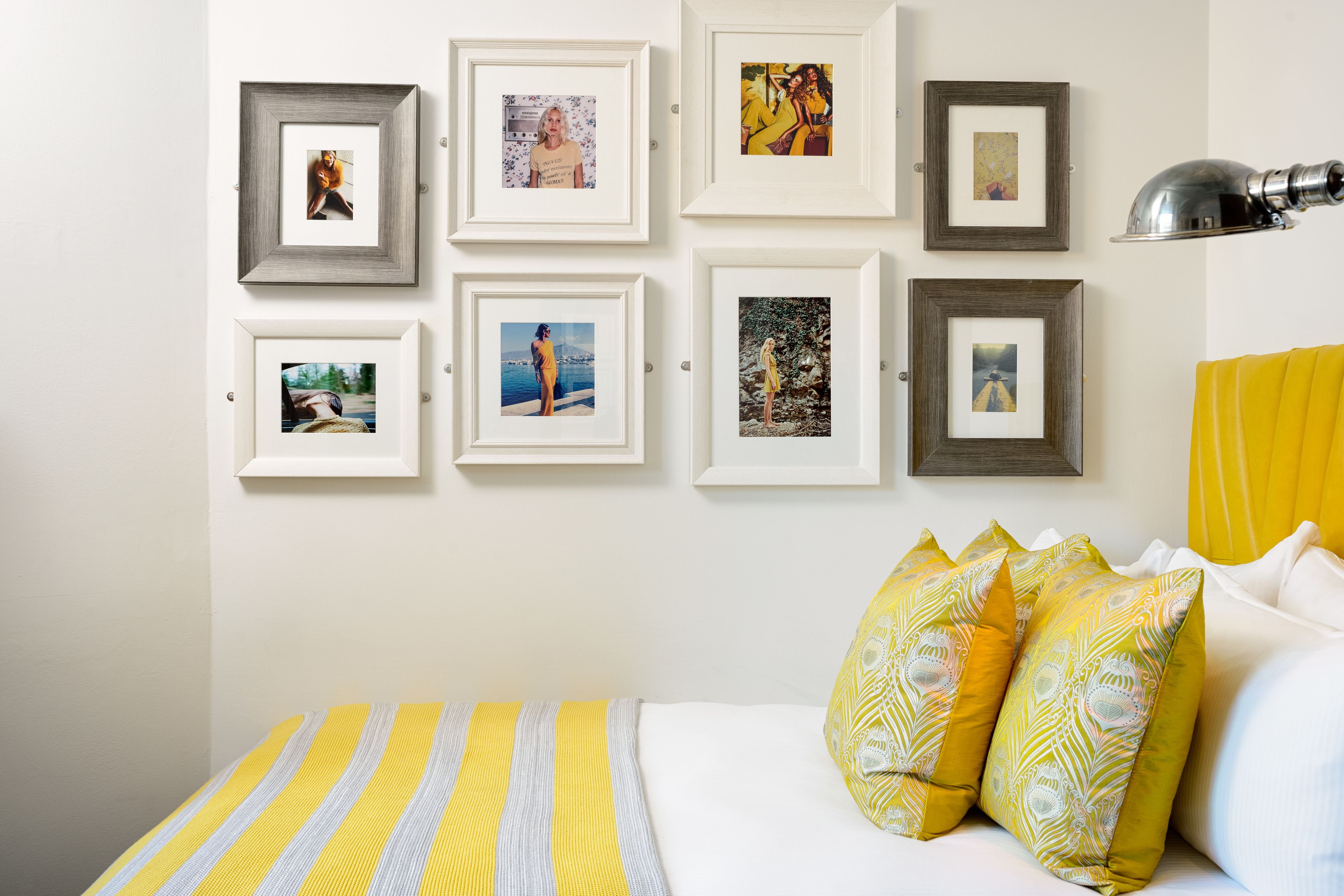 Een slaapkamer met een bed, kussens en een muur met ingelijste foto's.