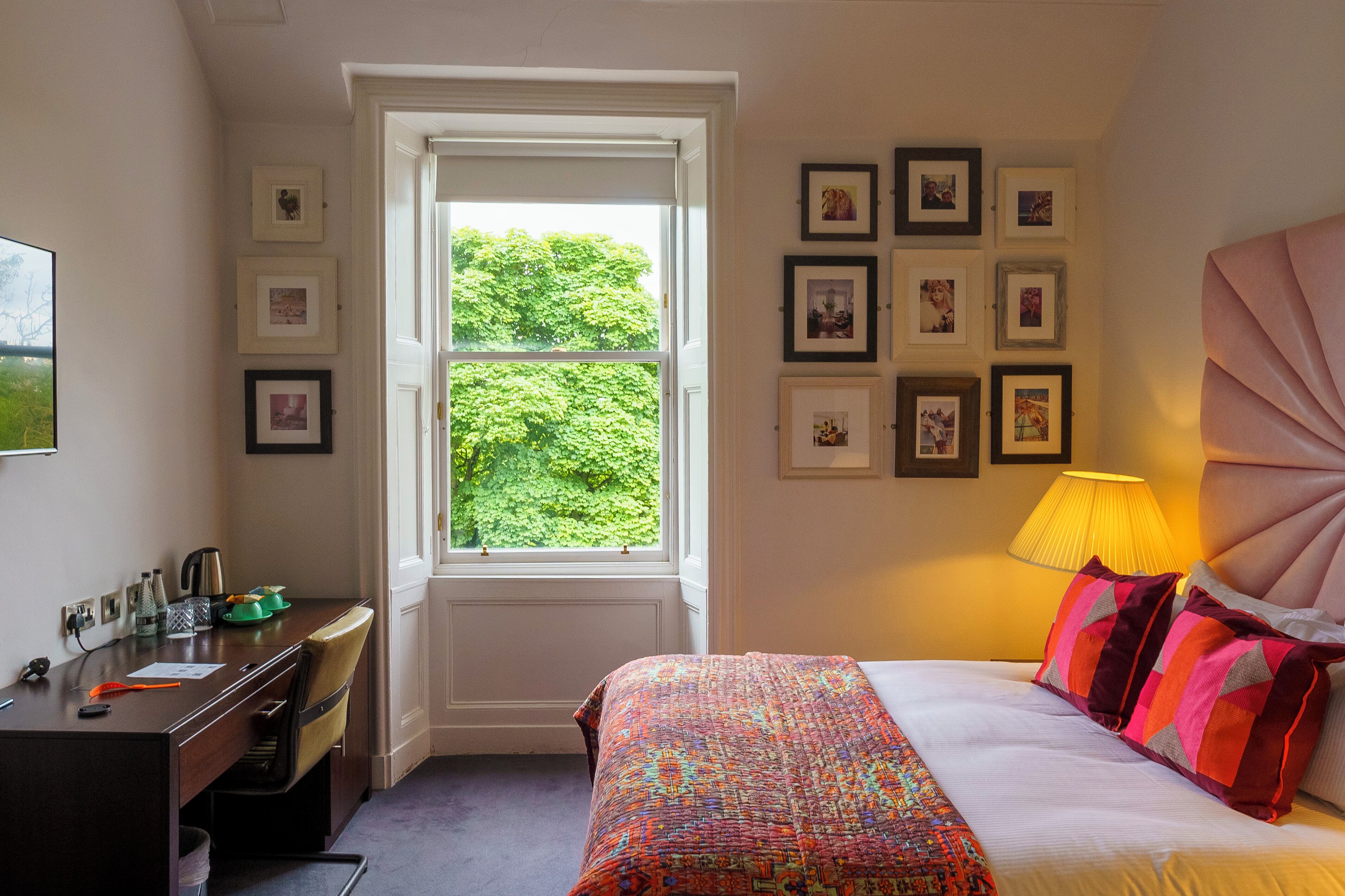 A bedroom with a bed, a desk, and a window with a view of greenery.