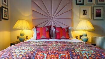 Un lit avec une couverture colorée, deux lampes de chevet et une tête de lit décorative.