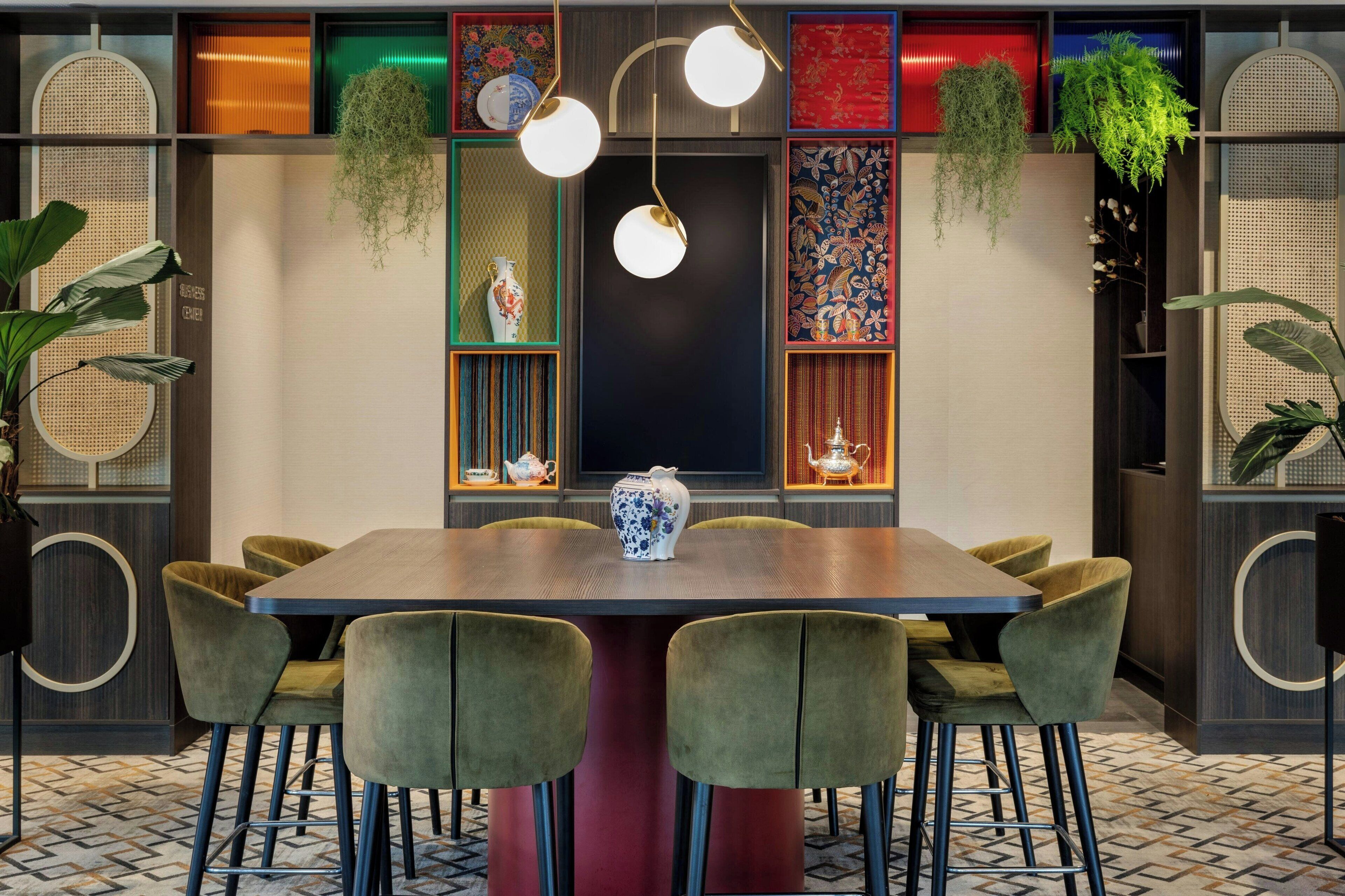 A dining area with a wooden table, green upholstered chairs, hanging plants, and decorative items on shelves.