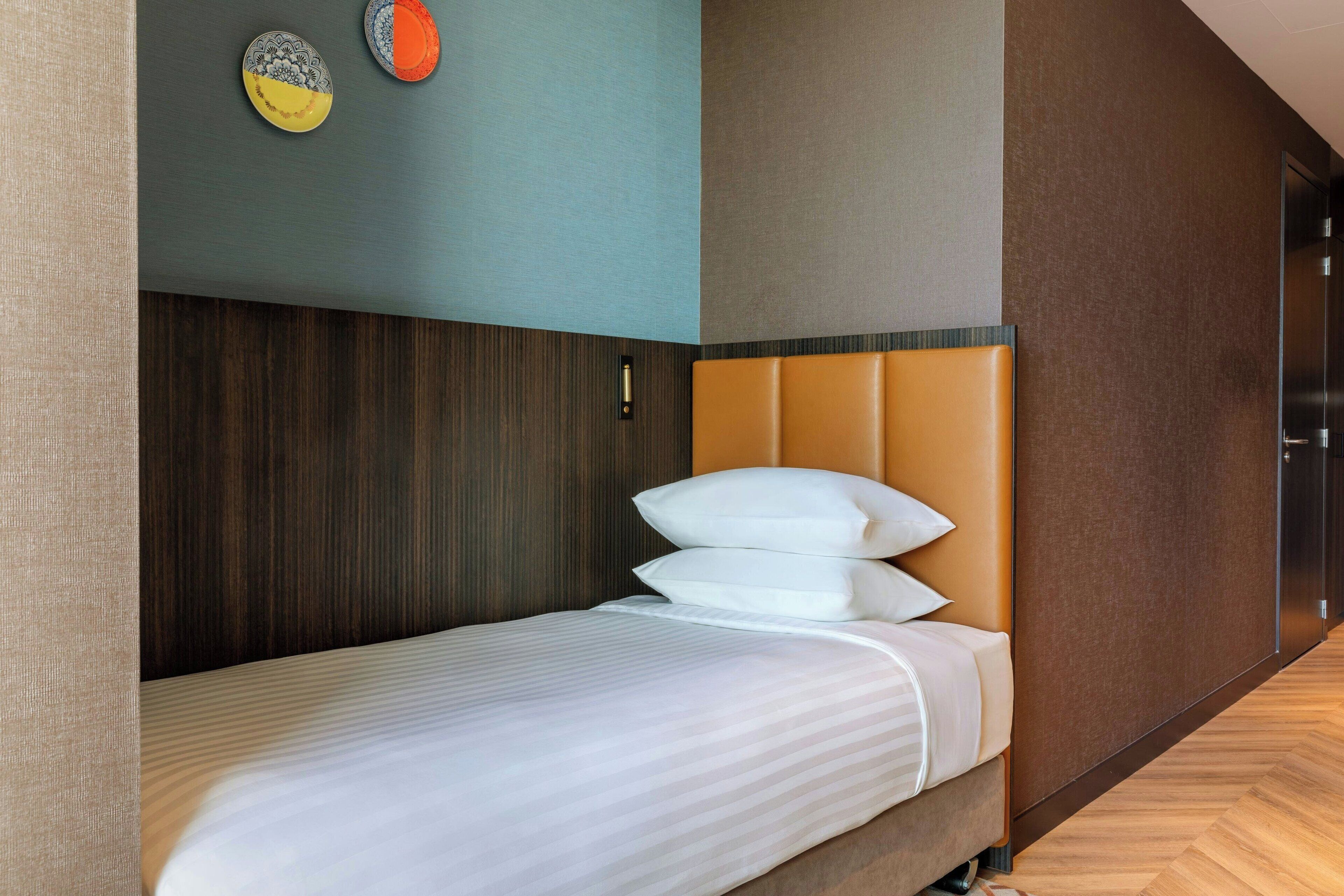 Una cama bien hecha con cabecera, un reloj de pared y dos placas decorativas en la pared.