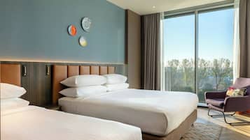 Una habitación de hotel moderna con dos camas, un ventanal con vistas y una silla con cojín.