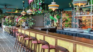 A bar area with a long counter, multiple stools, and a variety of plants and decorations. - Corendon Amsterdam New-West, a Tribute Portfolio Hotel (Amsterdam)