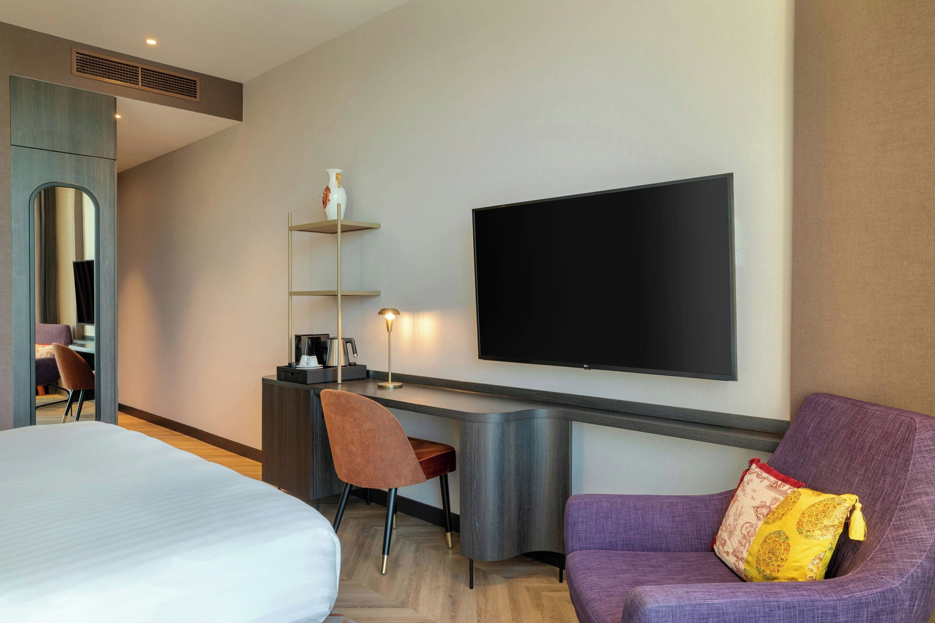 Une chambre d’hôtel comprenant un lit, un bureau avec une chaise, un téléviseur à écran plat et un canapé.