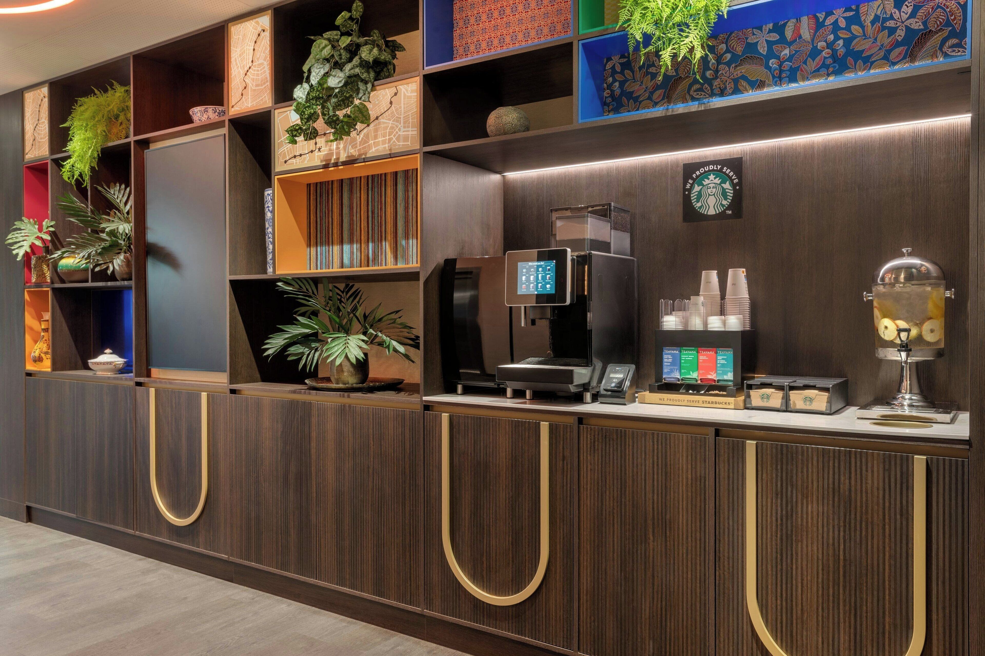 Un espace d’accueil moderne, doté d’une machine à café, du logo de Starbucks et d’une présentation de plantes.