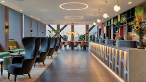 A modern hotel lobby with a long reception desk, comfortable seating, and a view of the outdoors. - Corendon Amsterdam New-West, a Tribute Portfolio Hotel (Amsterdam)