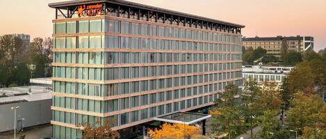 A modern hotel building with a glass facade, multiple floors, and a prominent sign at the top.