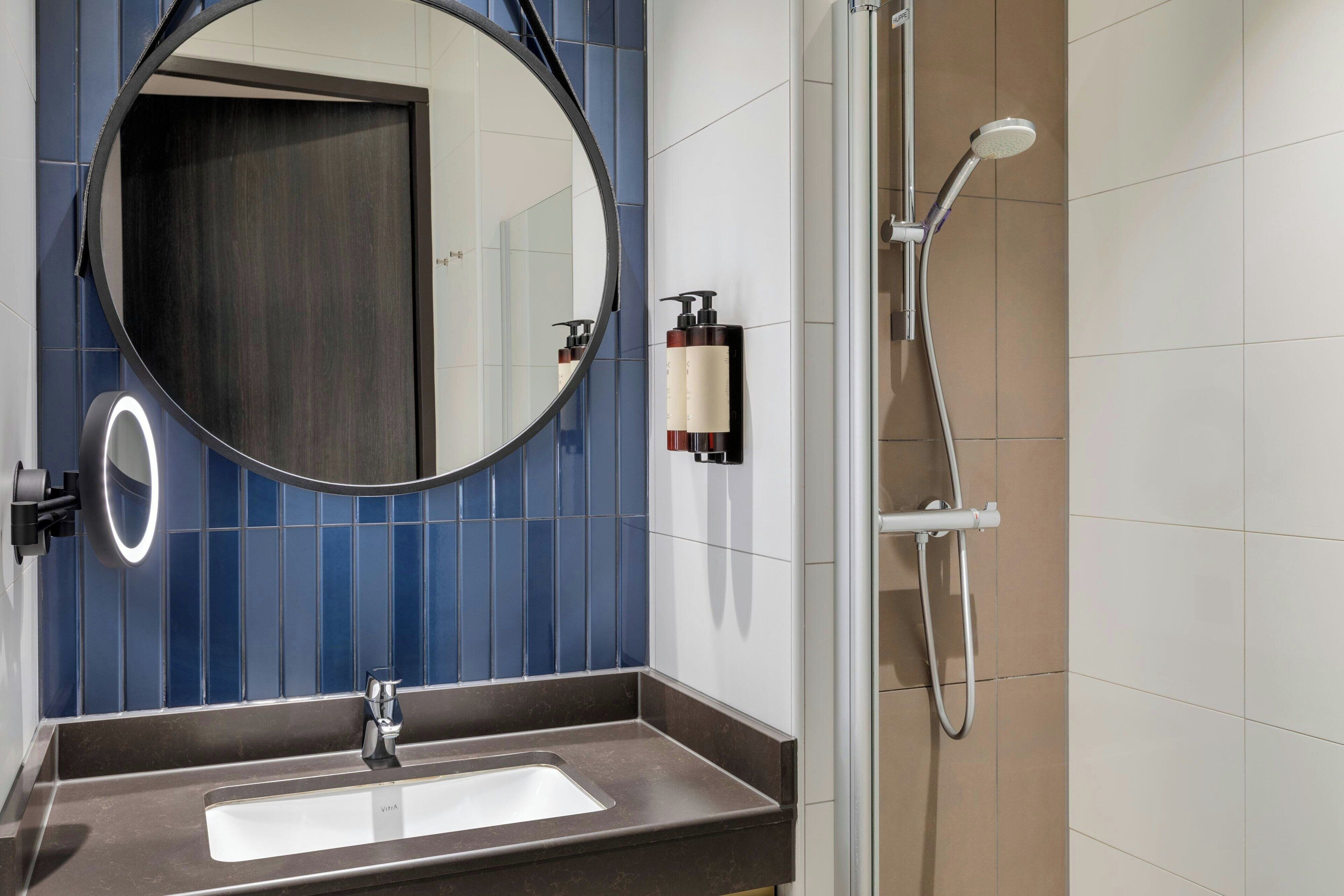 A bathroom with a round mirror, a sink, and a shower.