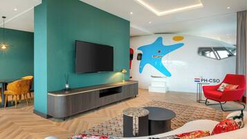 Un salon moderne avec un mur de couleur turquoise, un téléviseur à écran plat, un fauteuil rouge et une œuvre d’art murale originale.
