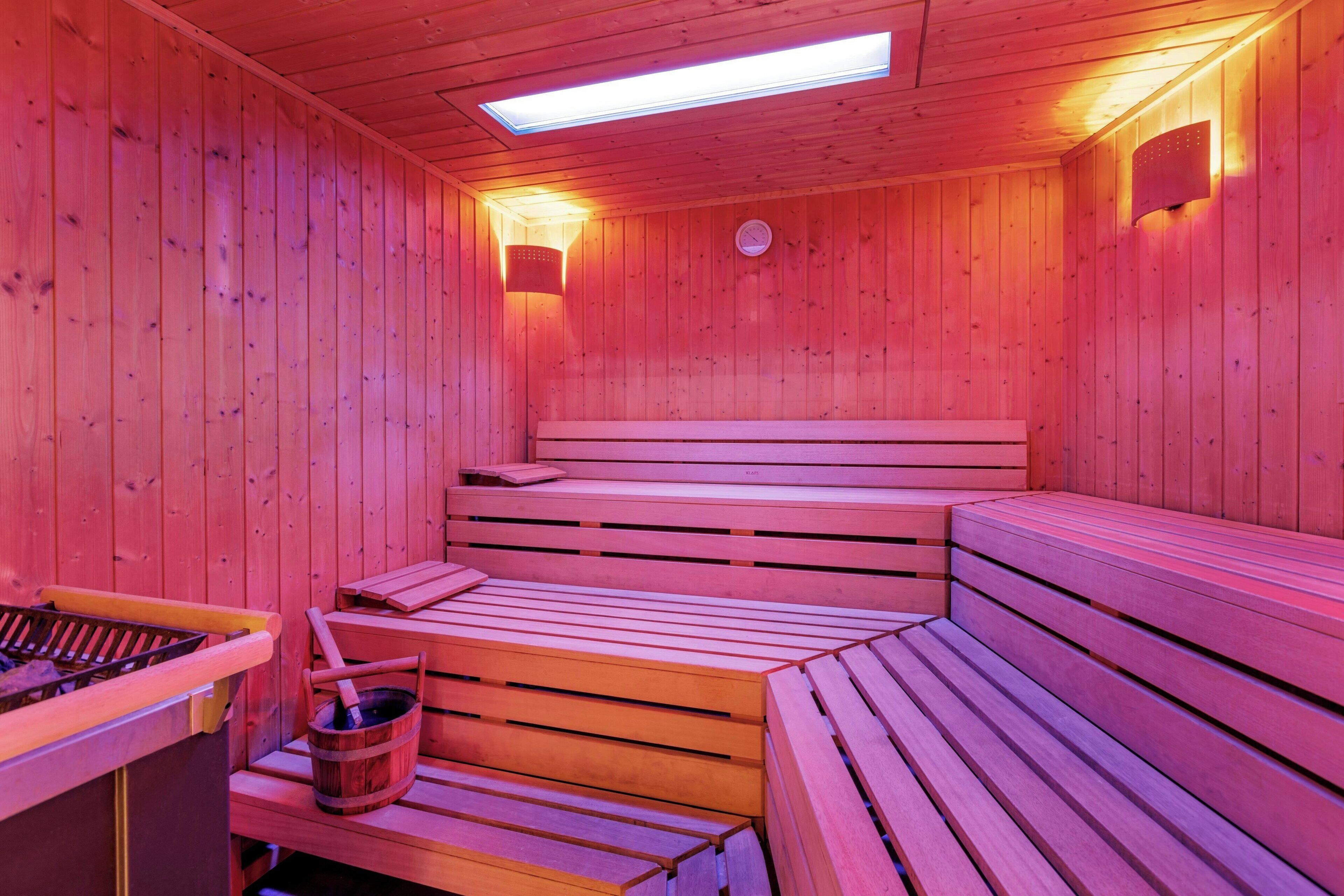 A sauna with wooden benches and a bench seat, a wooden bucket, and a heater.