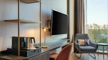 Una habitación de hotel moderna con un televisor de pantalla plana montado en la pared, un escritorio con cafetera, una silla y una mesita.