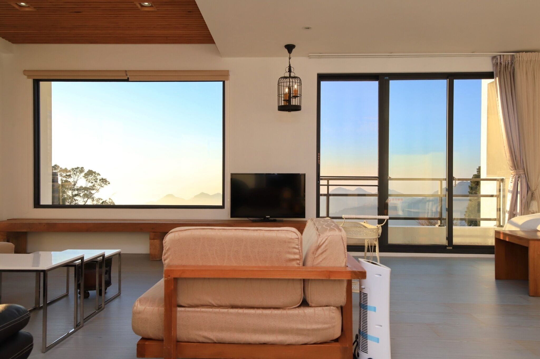 Una sala de estar moderna con sofá, televisor y grandes ventanales que ofrecen vistas a las montañas.