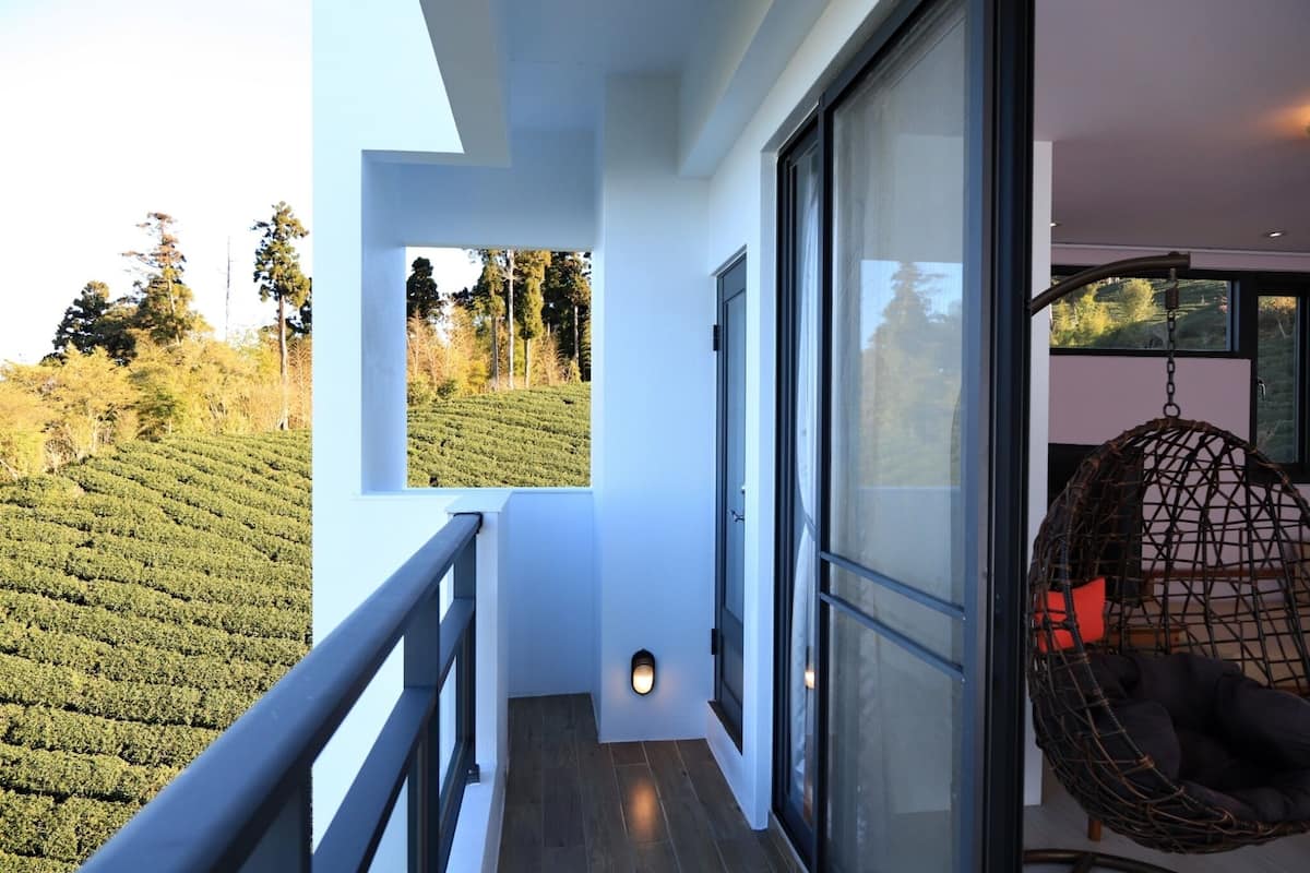 Un balcon donnant sur une plantation de thé, un fauteuil suspendu et un intérieur moderne avec de grandes fenêtres.