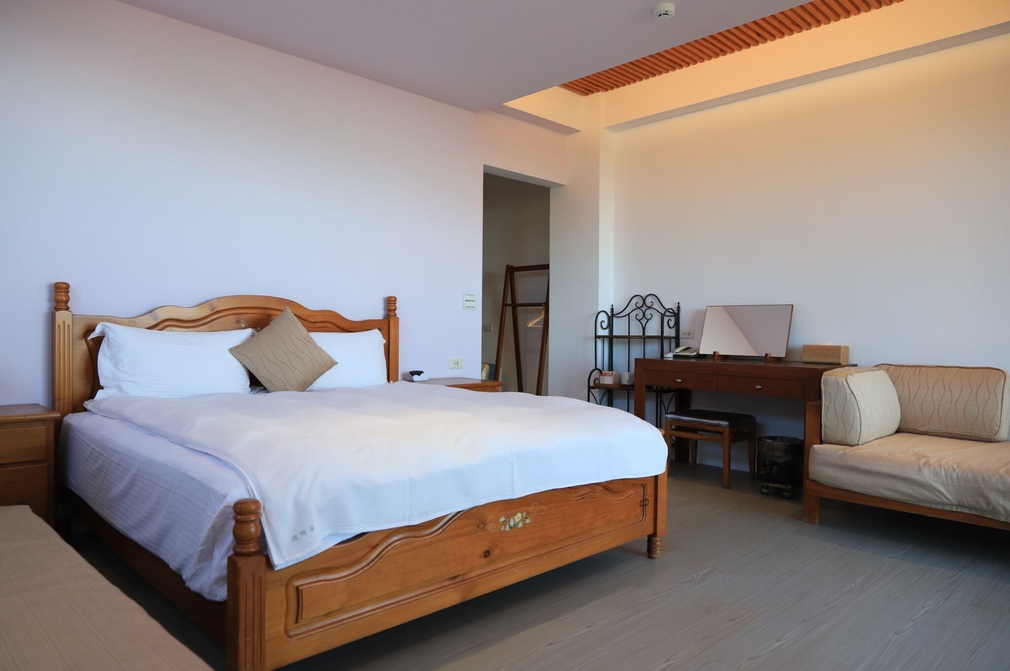 A bedroom with a wooden bed, a desk, a chair, and a sofa.