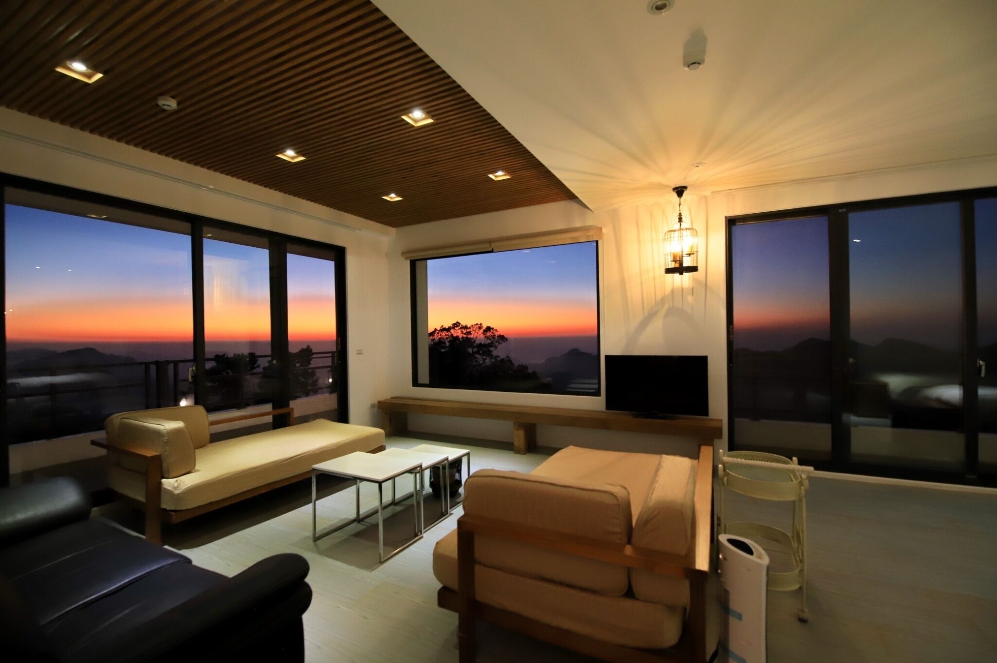 Una sala de estar moderna con ventanas amplias, un sofá, una mesa de centro y un televisor.
