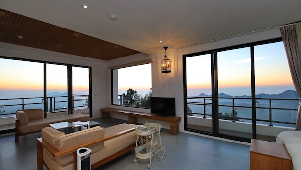 A spacious living room with a sofa, a coffee table, and a TV on a balcony overlooking a scenic view. - Alishan B&B Yunmingi Aliscenery (Zhuqi)
