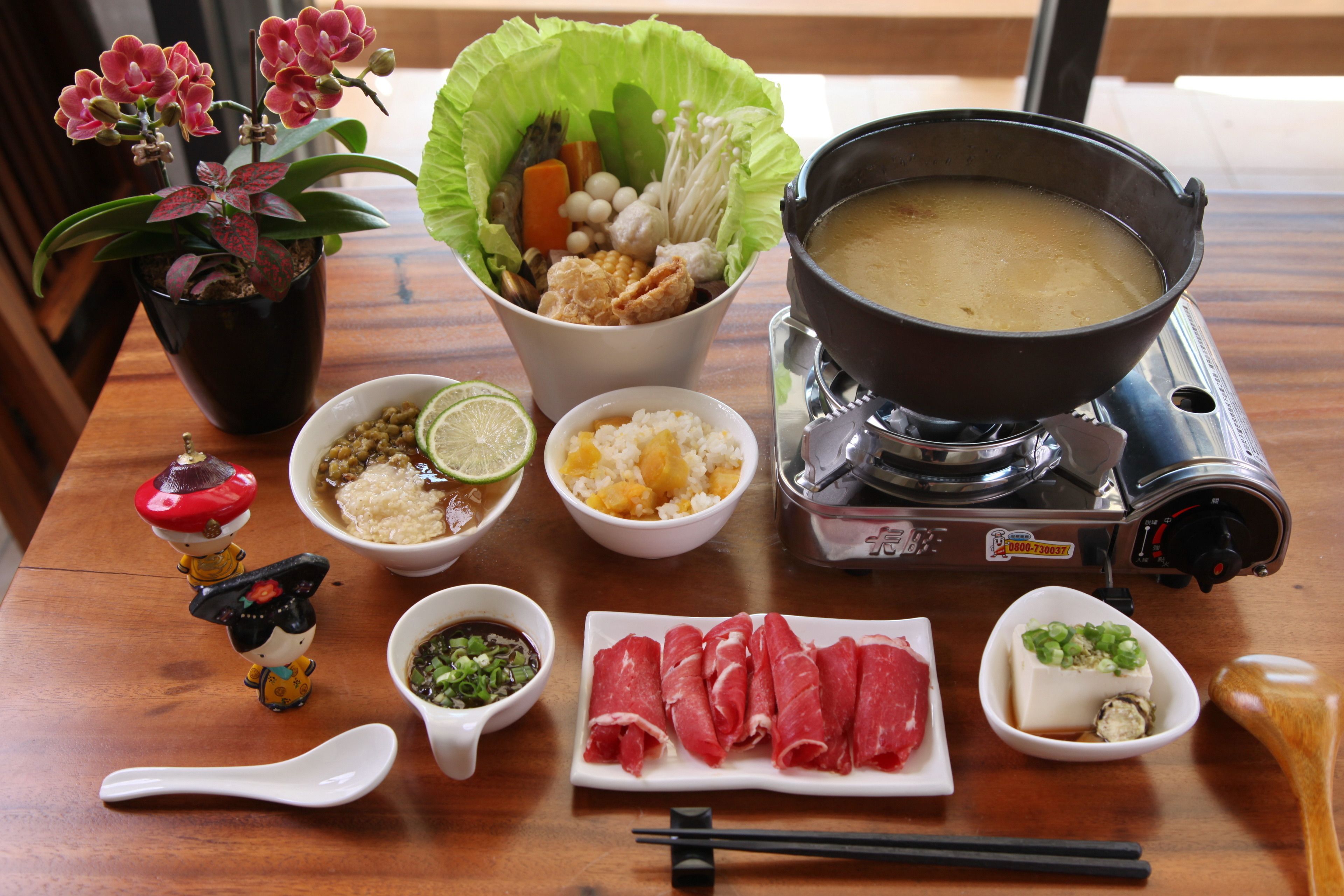 A dining table with various dishes, including a hot pot, sashimi, and a potted plant.