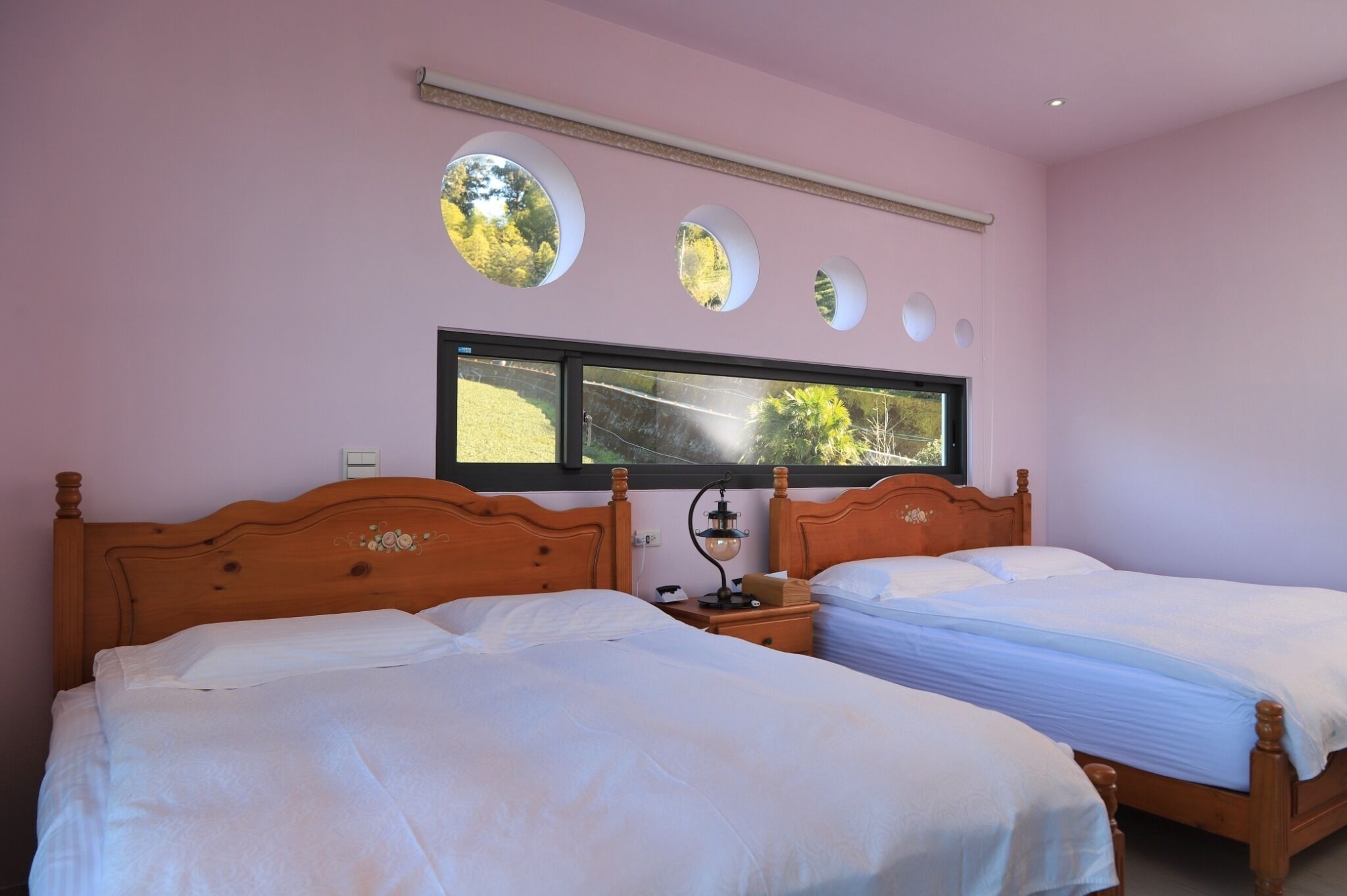 A bedroom with two beds, a window with a view of greenery, and circular wall decorations.