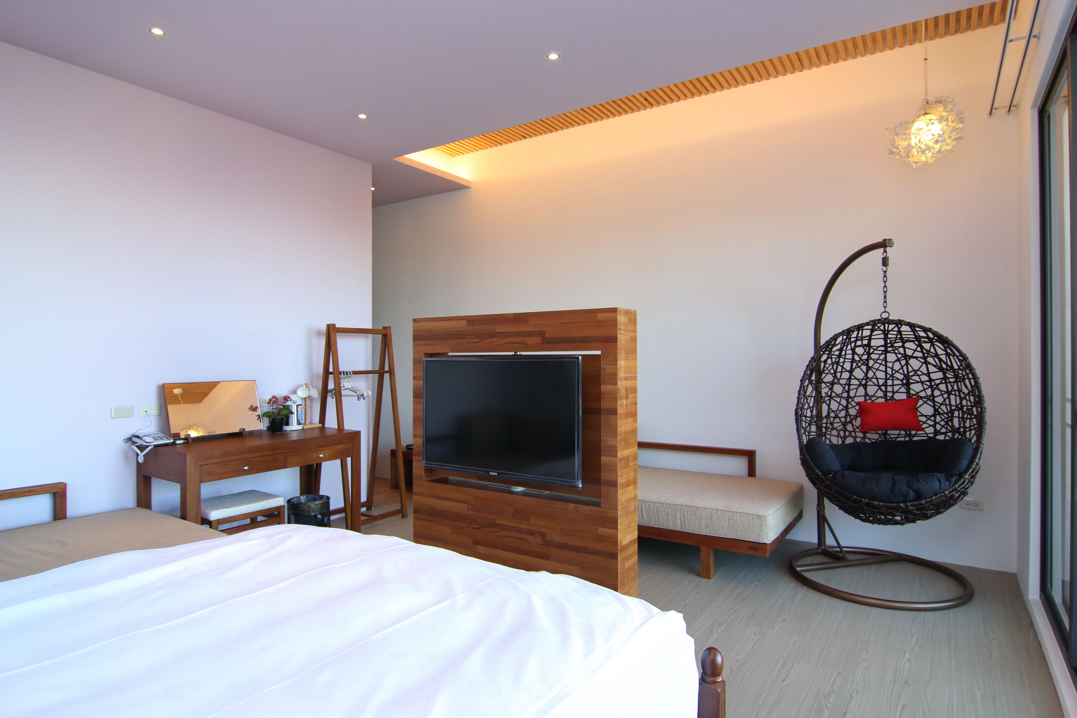 A modern hotel room with a large bed, a wooden desk with a flat-screen TV, a hanging chair, and a large window.