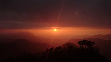 Ein Sonnenuntergang über einer Bergkette, im Vordergrund Silhouette von Bäumen.