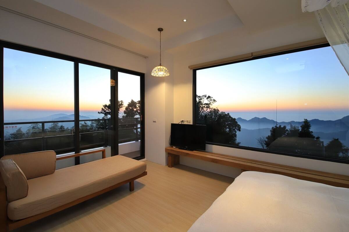 Une chambre d’hôtel moderne dotée d’un grand lit, d’un canapé, d’un téléviseur posé sur un meuble et de grandes fenêtres offrant une vue sur les montagnes.