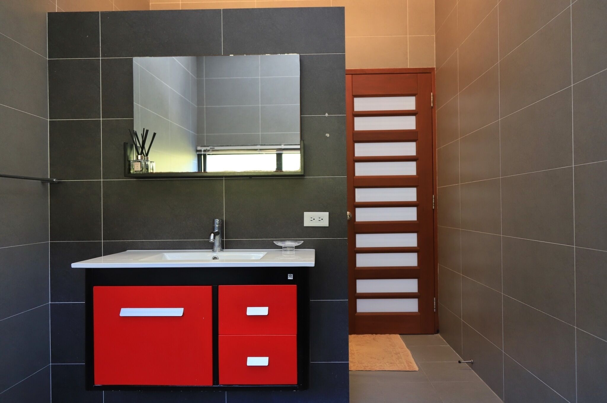 A modern bathroom with a large mirror, a sink, and red cabinets.
