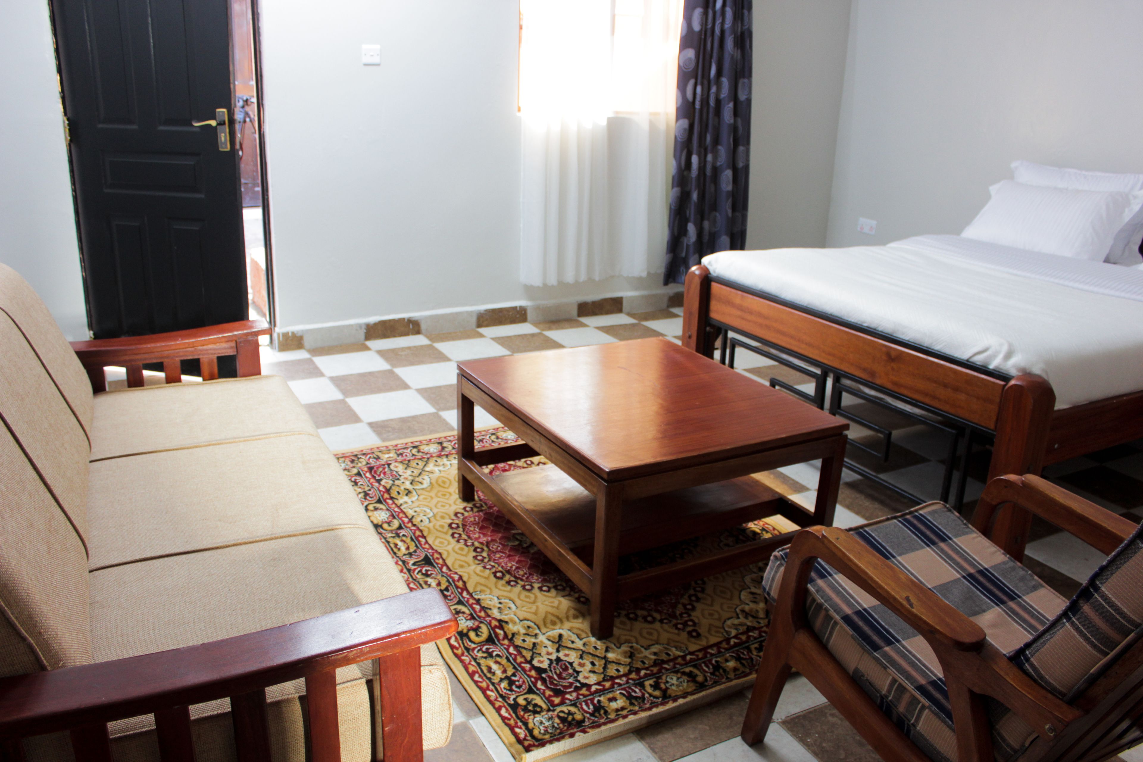 A hotel room with a bed, a sofa, a wooden table, and a patterned rug.