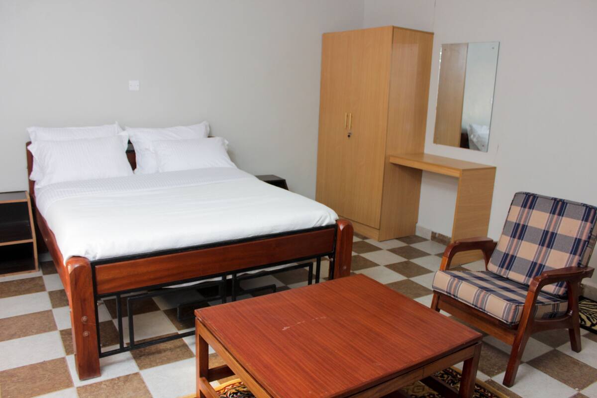 A room with a bed, a wooden wardrobe, a chair, and a small table.