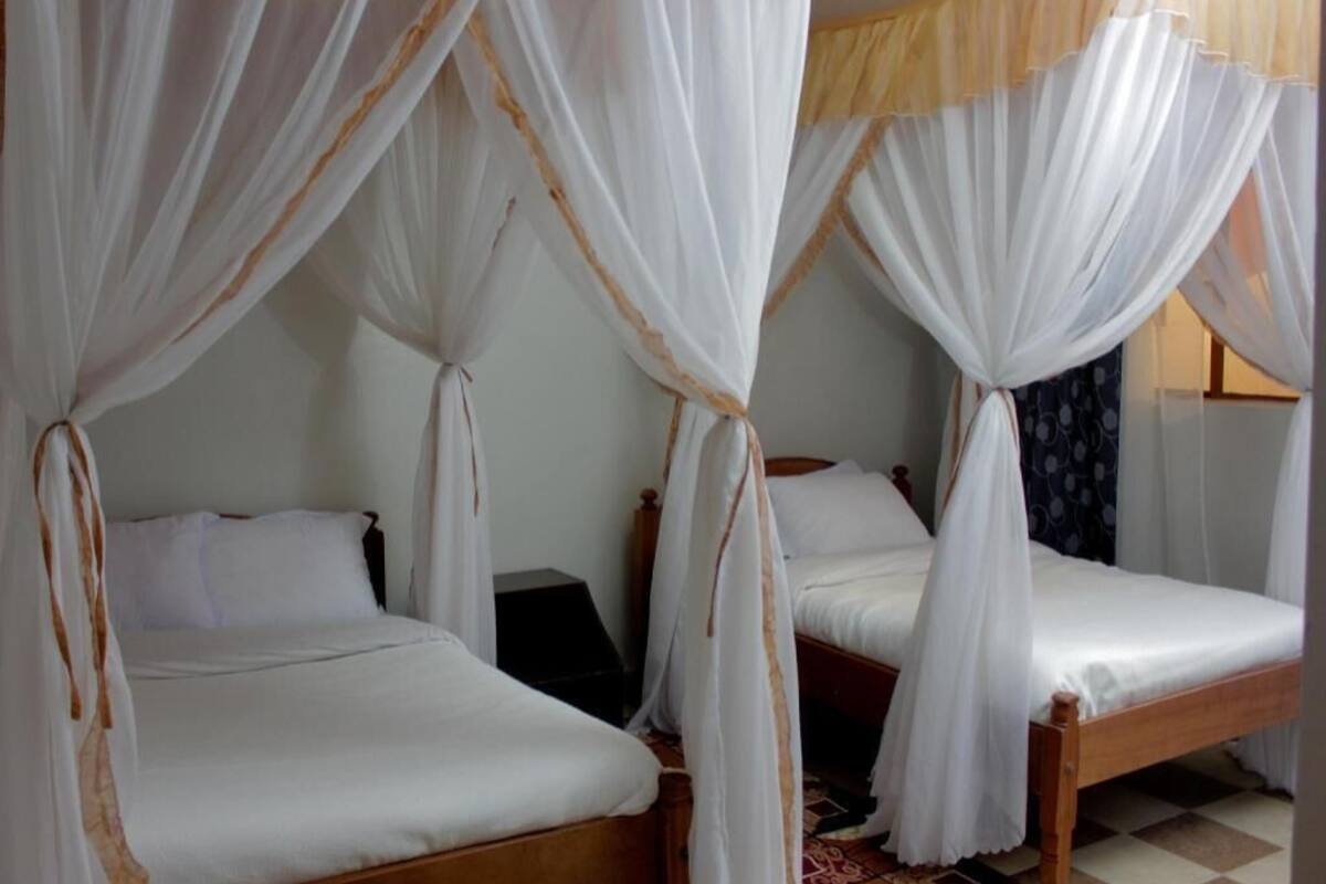 A room with two wooden beds, each with a canopy bedspread.
