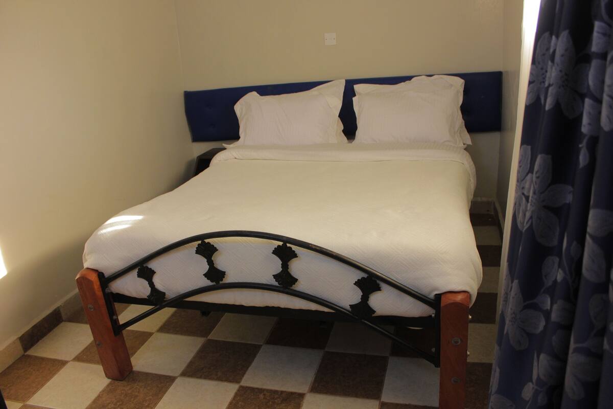 A single bed with a wooden frame and a headboard, a checkered floor, and a plain wall.