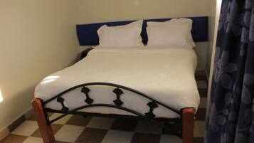 A single bed with a wooden frame and a headboard, a checkered floor, and a plain wall.