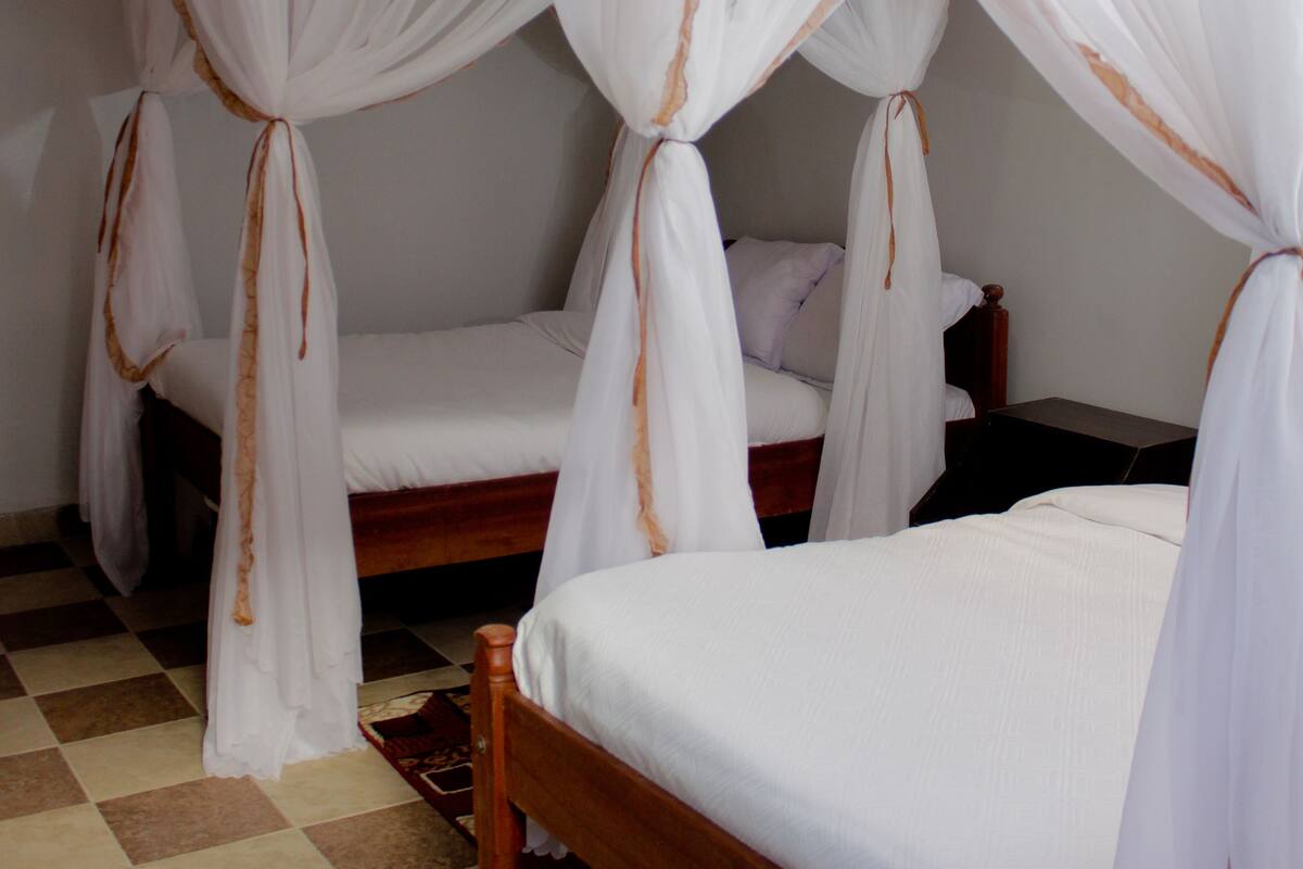 A room with two beds, each with a canopy. The room has a checkered floor and a wooden headboard.