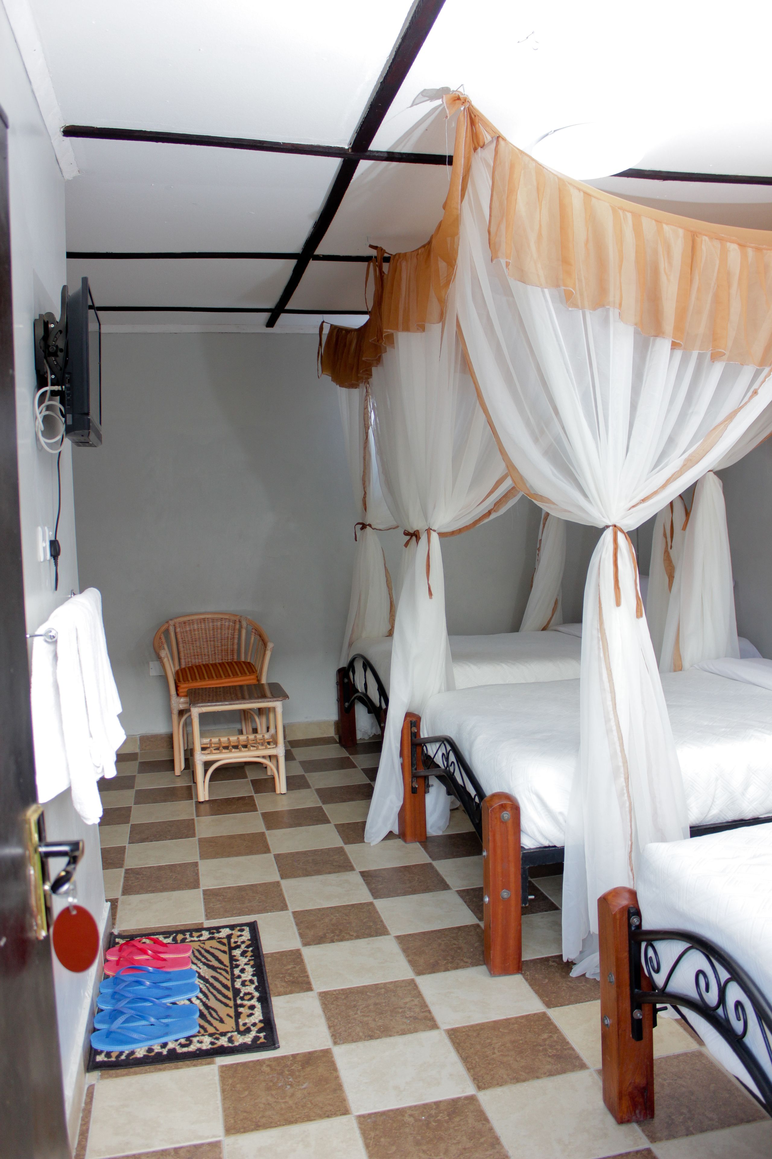 A room with a checkered floor, a bed with a canopy, a chair, and a small table.
