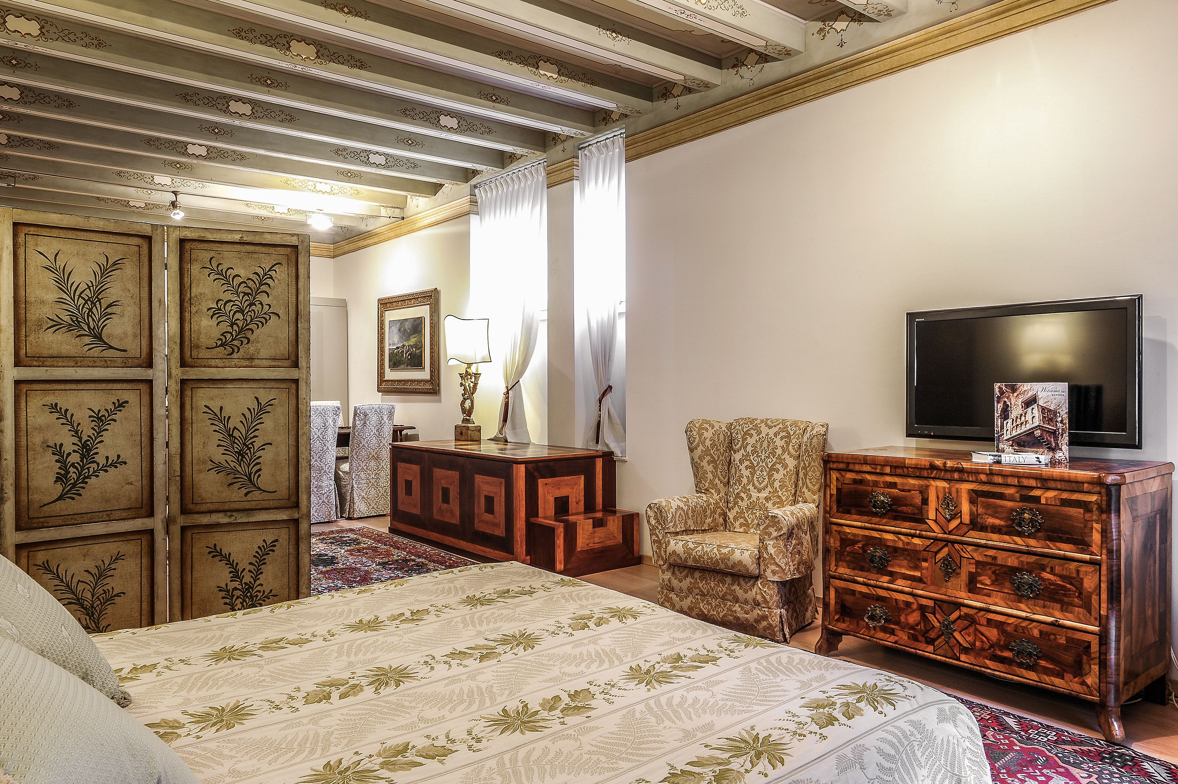 Une chambre à coucher avec un lit, une commode en bois, une chaise et un téléviseur.