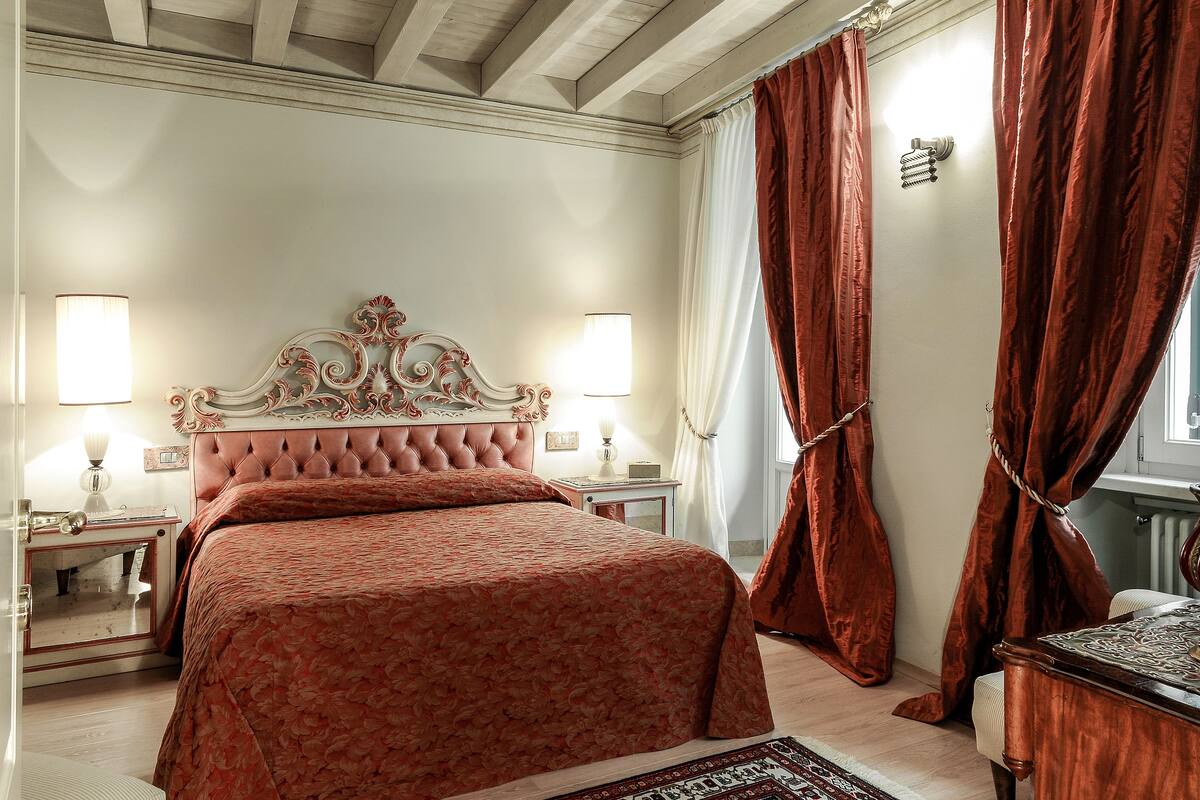 Un dormitorio con una cama grande, dos mesitas de noche, una cómoda y un ventanal con cortinas.