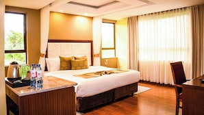 A hotel room with a large bed, a desk with a kettle, two bottles of water, and a chair. - Lake Naivasha Resort (Naivasha)