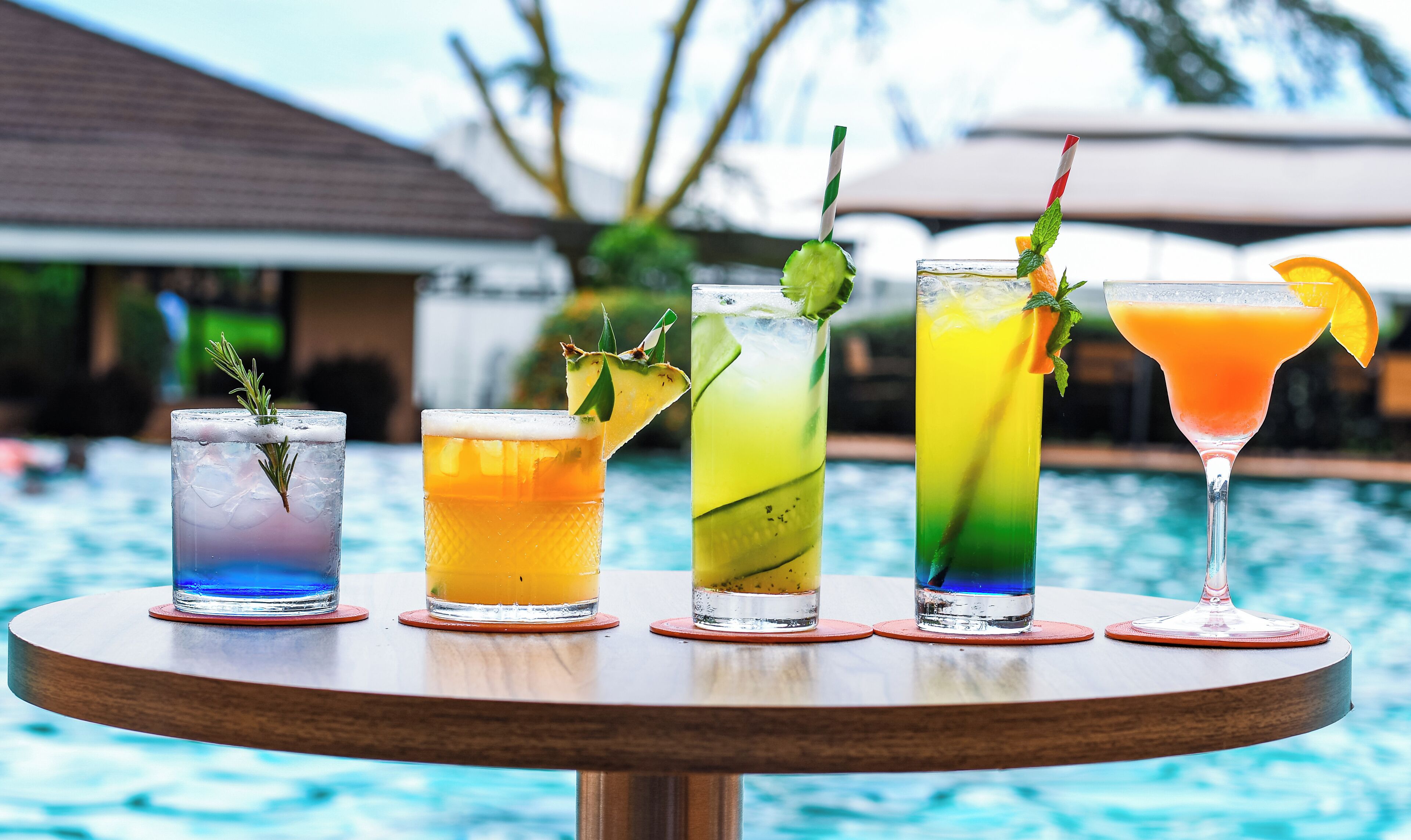 Una mesa con cinco bebidas, una piscina y un edificio al fondo.