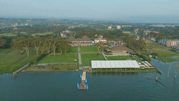 An aerial view of a lakeside property with a large building, a dock with boats, and surrounding greenery.