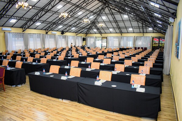 A large hall with rows of tables and chairs, a high ceiling with structural beams, and a wooden floor.